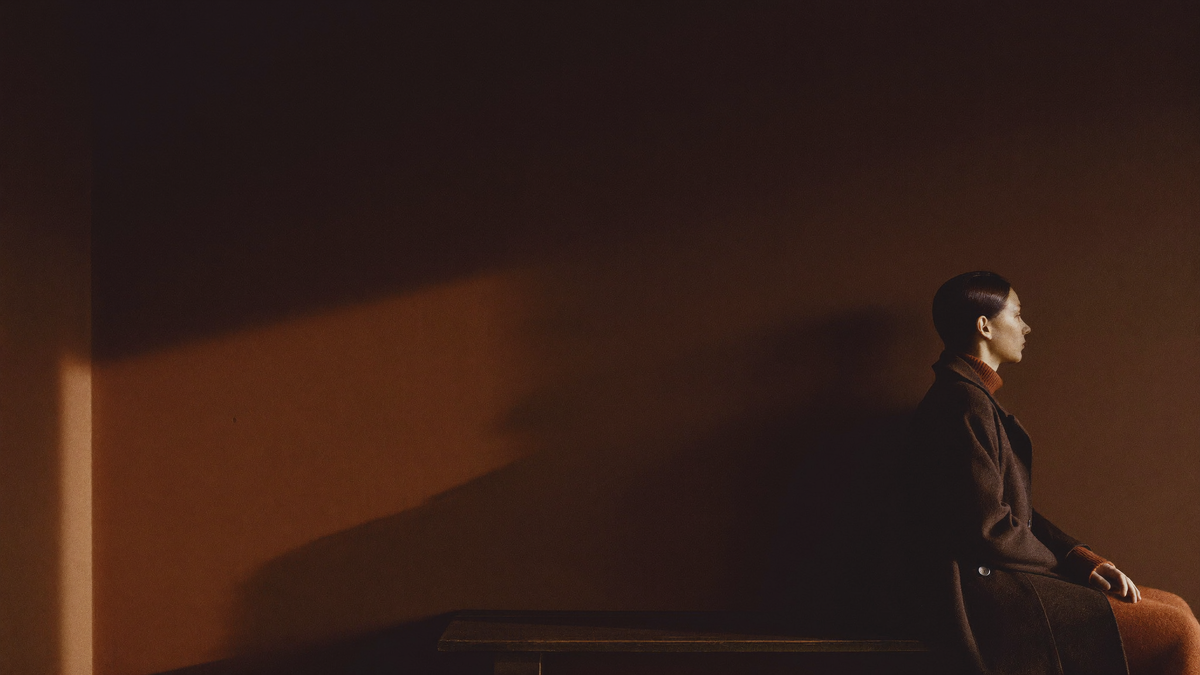 Figure in dark wool coat at dusk, warm light band across the wall