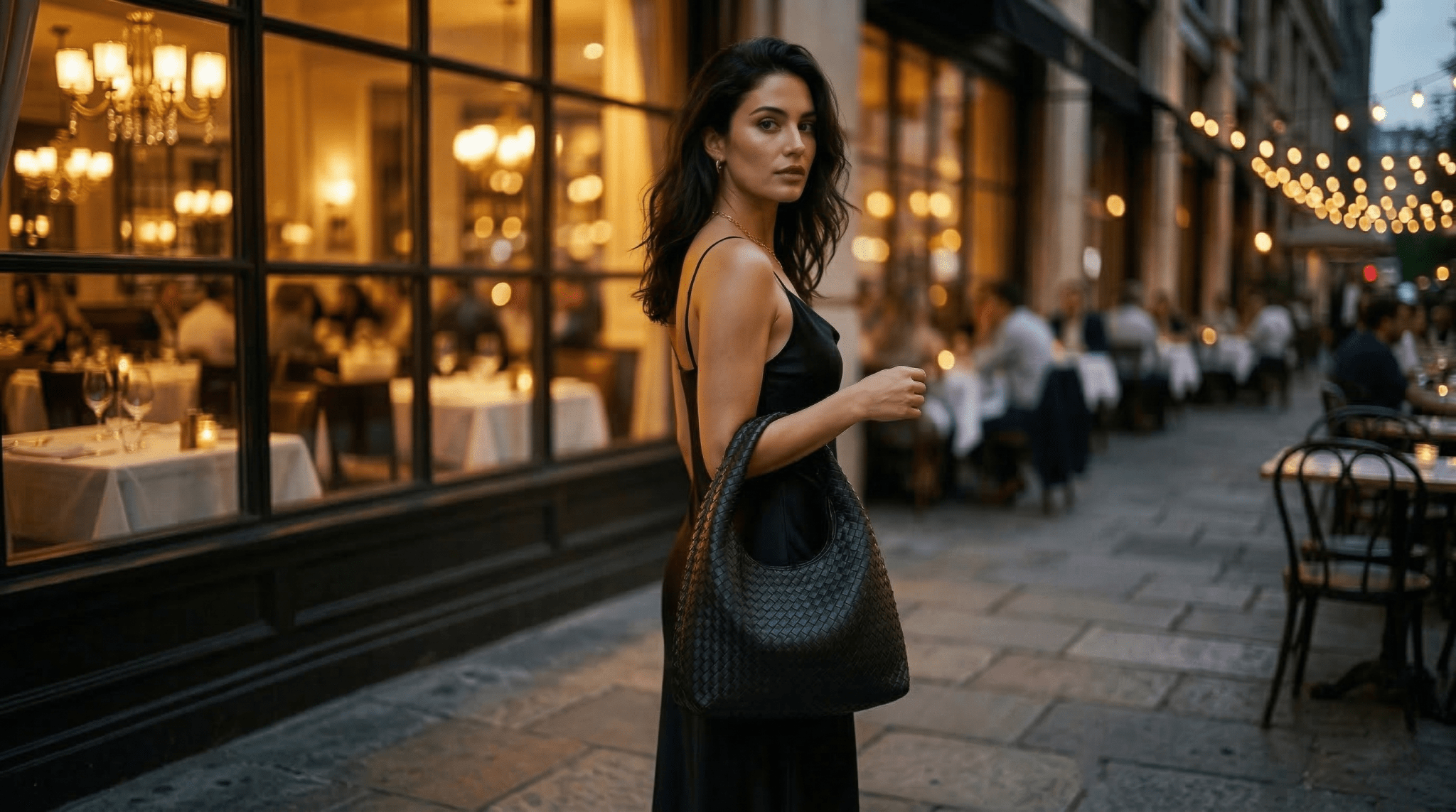Woman in a black dress standing on a city street with restaurant exterior in the background