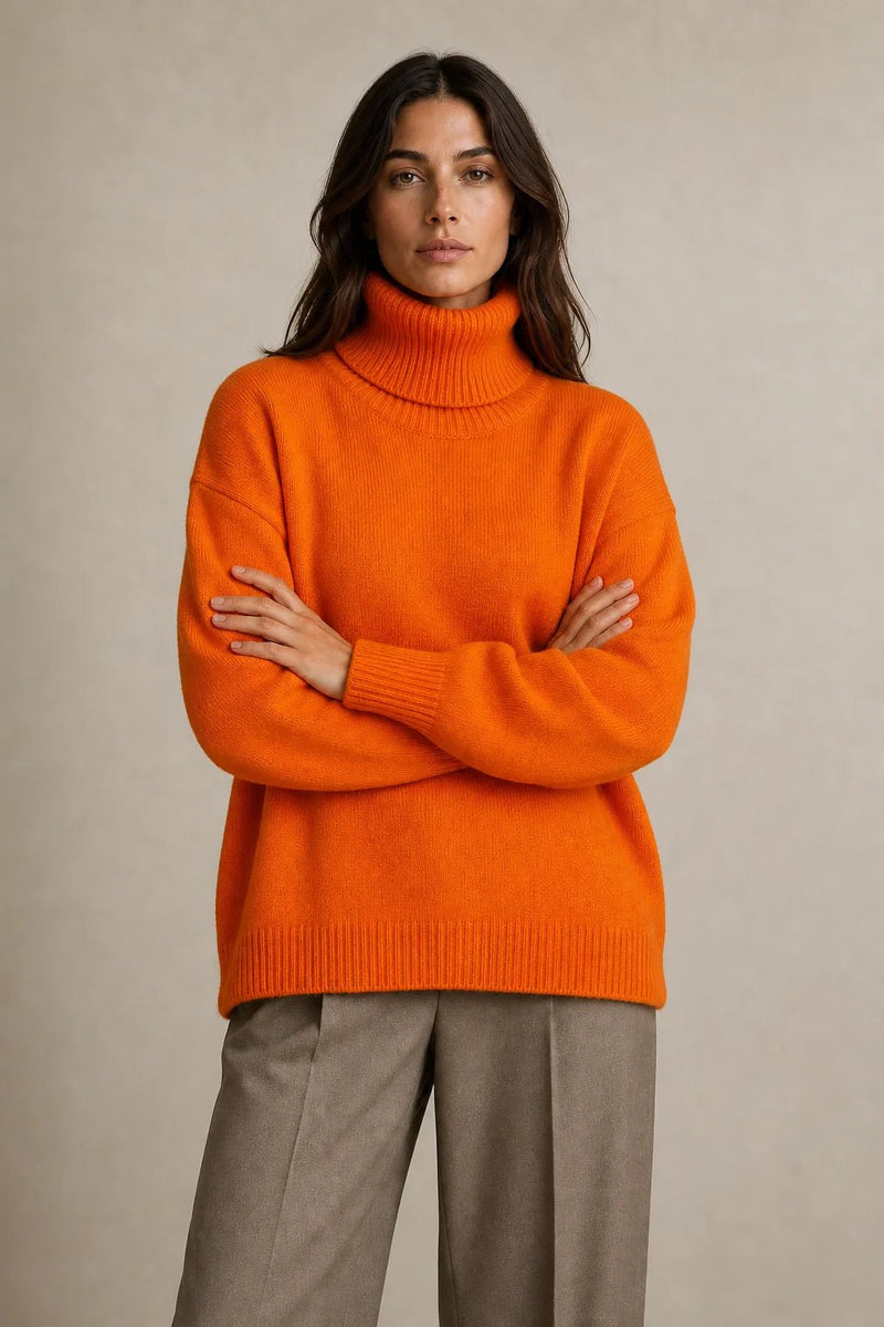 Sofaine Nova oversized knit turtleneck sweater in bright orange, worn front view with arms crossed