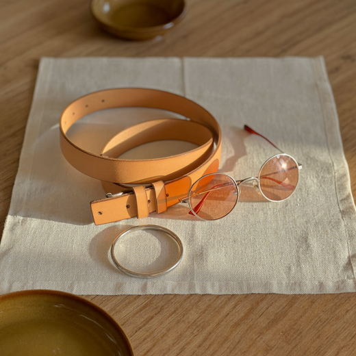 Leather belt, sunglasses and bangle still life on linen