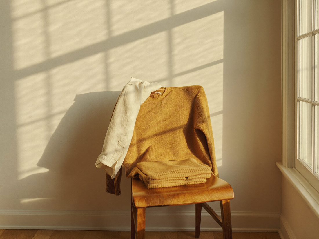 Linen shirt and camel knit over a wooden chair in window light