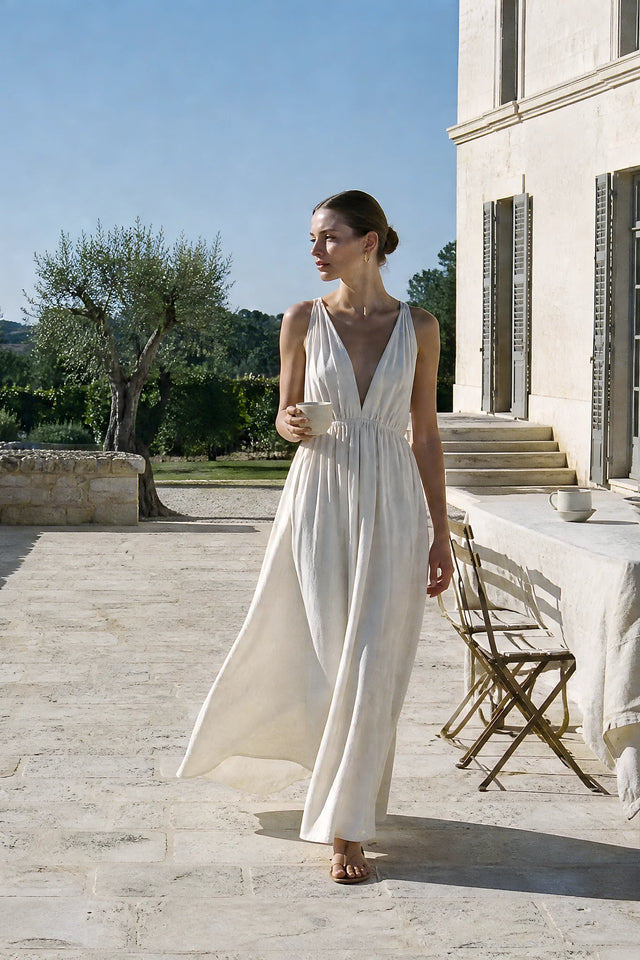 Woman in a flowing ivory maxi dress on a sunlit stone terrace